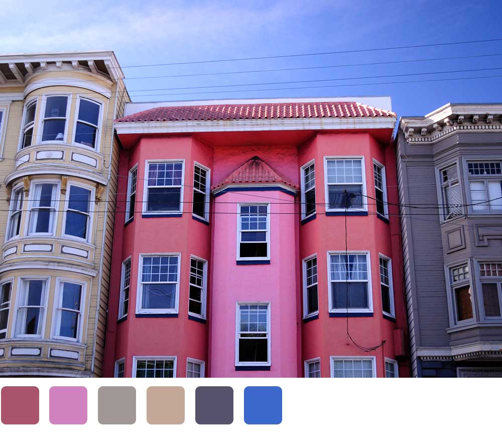San Francisco Victorians, one bright pink, one beige, one gray, and blue sky above the houses